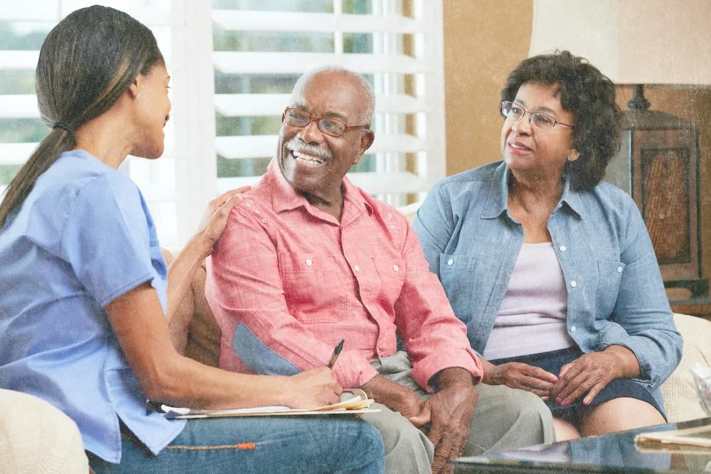 A carer sitting with an elderly couple at home, discussing their care plan warmly
